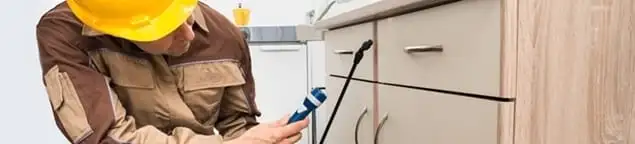 Roach exterminator applying treatment under kitchen cabinets in Ann Arbor, MI